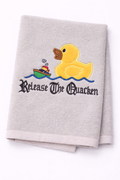 Gray towel with a rubber duck and boat design and text 'Release The Quacken' on a white background